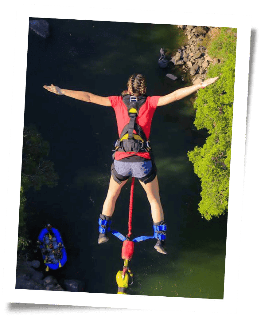 kaila bungee jumping from above into a river with a raft passing by below